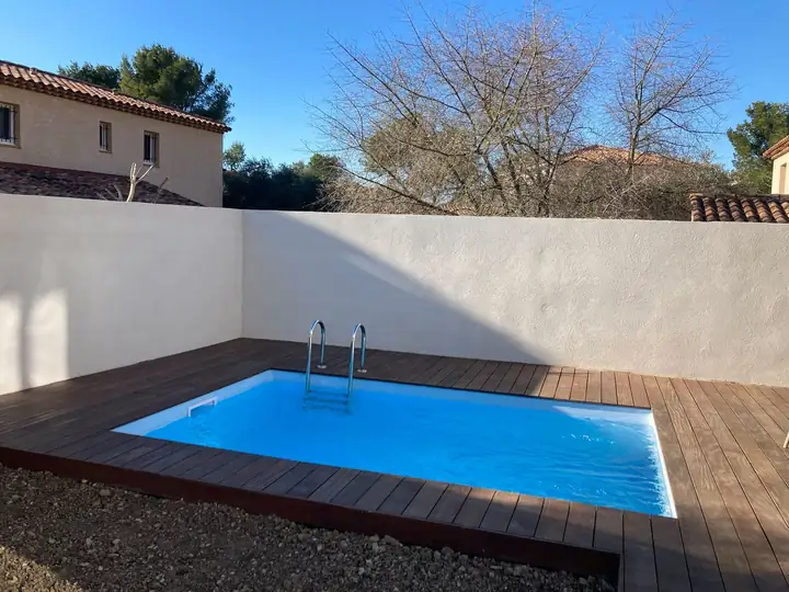 Piscine avec plage en bois et murs de clôture enduits